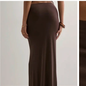 Brun långkjol i stretchigt material - Snygg brun långkjol med tight passform och minimalistisk design. Kjolen är figurnära och har en mjuk, stretchig känsla som gör den superbekväm. Perfekt att styla med crop tops eller oversized tröjor för en trendig look.