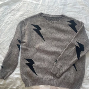 Grå stickad tröja med blixtar - Grå stickad tröja med svarta blixtmönster på både fram- och baksida samt ärmar. Rund halsringning och ribbade muddar vid ärmslut och nederkant. Perfekt för dig som gillar en cool och unik look.                                                                     Köpt från Shein.