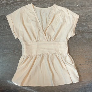 blus - Supersöt beige omlottopp med v-ringning och  markerad midja. Den sitter jättefint i midjan och passar jättebra till jeans eller kjol! 😍