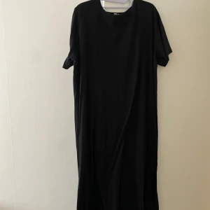 Svart långklänning från ASOS - Enkel och stilren svart långklänning från ASOS i rak modell med rund halsringning och korta ärmar. Klänningen är tillverkad i mjuk bomull och passar perfekt för en avslappnad och cool look. 