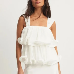 Volangtopp från NA-KD i vitt - Säljer denna vita toppen från den eftertraktade Lovisa Wallin kollektionen från Na-kd! Den är i nyskick, aldrig använd enbart testad. Sett att folk säljer denna för 400 kronor (500 nypris) men jag säljer för 350!🤍