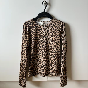 Leopardmönstrad långärmad topp H&M - Snygg långärmad topp från H&M med leopardmönster i beige och svart. Tight passform och rund halsringning, perfekt att styla med jeans eller kjol. Tillverkad i mjuk och stretchig polyester som sitter skönt mot kroppen.