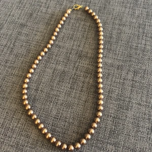 Bronsfärgat pärlhalsband - Snyggt halsband med runda pärlor i bronsfärg och ett litet guldfärgat spänne. Perfekt accessoar för att lyfta din outfit med en klassisk touch. Pärlorna är jämnt placerade och ger ett stilrent intryck. Hör av dig om du har några funderingar eller vill ha fler bilder! 