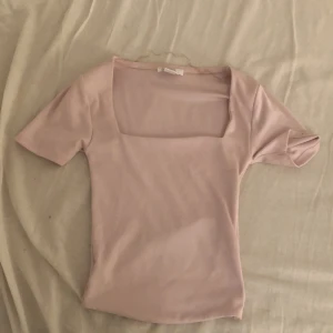 Ljusrosa topp med fyrkantig ringning Amisu - Supersöt ljusrosa topp från Amisu med korta ärmar och snygg fyrkantig ringning. Modellen är figurnära och passar perfekt till jeans eller kjol. Mjuk och stretchig känsla i materialet gör den riktigt bekväm att bära.