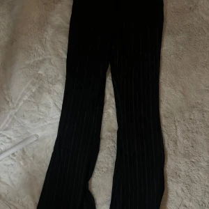 Svarta randiga byxor Urban Outfitters - Svarta byxor från Urban Outfitters med tunna vita ränder. Klassisk rak passform med fickor och snyggt skräddad look. Perfekta för dig som gillar stilrena och trendiga plagg med lite edge. Aldrig använda 