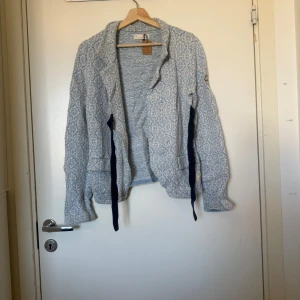 Odd Molly ljusblå cardigan jacka - Säljer en ljusblå och vit kofta med snyggt geometriskt mönster. Jackan har långa ärmar, knytband i mörkblått och dekorativ kompassdetalj på ena ärmen. Perfekt för dig som gillar unika detaljer och skön passform. Från märket Odd Molly i storlek 2 som enligt deras storleksguide motsvarar en storlek M. Mer använd. Lösa trådar finns på insidan. den kan vara något tvätt påverkad. 