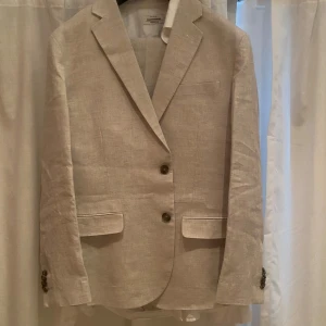 Beige linnékavaj Dressmann slim fit - Snygg beige kavaj från Dressmann i 100% linne, slim fit-modell. Klassisk design med två knappar framtill, fickor med lock och knappar vid ärmslut. Perfekt för en fräsch och stilren look under varmare dagar. Nypris = 2199kr mitt pris = 1400kr endast använd 2 gånger!!!! Inga defekter eller spår av användning! 🌸