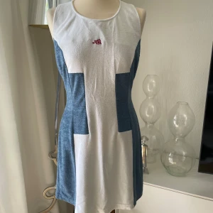 Kana Beach blåvit frottéklänning - Superskön blåvit kortklänning från Kana Beach i frotté. Ärmlös modell med sportig racerback och coola färgblock. Perfekt för strandhäng eller chill dagar. Liten röd logga framtill och dragkedja i ryggen. Sitter snyggt och har en avslappnad vibe. Storlek är mindre M 