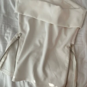 Vit axelbandslös topp från Zara - Snygg vit axelbandslös topp från Zara med raka linjer och två dragkedjor nertill på sidorna. . 