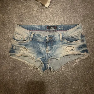 Blå slitna jeansshorts Tally Weijl - Snygga blå jeansshorts från Tally Weijl med slitna detaljer och fransig kant. Modellen är lågmidjad och har klassisk femficksdesign. Perfekta för sommaren när du vill ha en avslappnad och cool look.