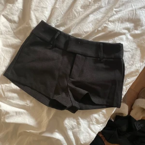 Svarta shorts med bred linning - Snygga svarta shorts med bred linning och hällor för bälte. Klassisk design med korta ben och diskret dragkedja framtill. Köpa på plick vet inte vart ifrån lappen är avklippt!