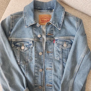 Klassisk jeansjacka  - Säljer en ikonisk ljusblå jeansjacka från Levi's med snygga silvriga knappar och två bröstfickor med lock. Jackan har klassisk krage och raka sömmar, perfekt för dig som gillar tidlös streetstyle. Passar lika bra till hoodie som till t-shirt.
