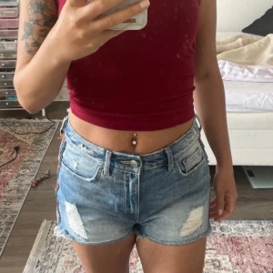 Snygga jeansshorts med brodyr - Snygga midwaist jeansshorts i ljusblå denim med slitna detaljer. Sidorna har en färgglad broderad bård i orange, rosa och grönt som ger en unik touch. Perfekta för sommardagar och festivalhäng. Fint skick. Storlek s. 50kr