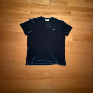 Svart t-shirt från Lacoste, L - Klassisk svart t-shirt från Lacoste i regular fit med korta ärmar och rund hals. Diskret Lacoste-logga med krokodil på bröstet. Skön och stilren modell i mjuk bomull, perfekt till jeans eller shorts.
