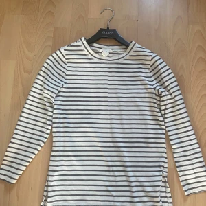 Randig långärmad tröja från H&M - Säljer en vit och mörkgrå randig långärmad tröja från H&M i storlek S. Tröjan har rund halsringning, raka ärmar och små slitsar i sidorna. Perfekt till jeans eller kjol för en chill och stilren look.