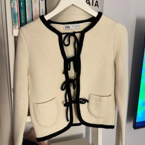 Beige kofta - Zara - Superfin beige stickad kofta från Zara med svarta kanter och knytning framtill. Koftan har två små fickor fram och långärmade ärmar.🥰