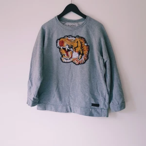 Grå sweatshirt med tiger Just Junkies strl S - Grå sweatshirt från Just Junkies med en stor broderad tiger i orange, svart och vitt på bröstet. Tröjan har rund hals, långa ärmar och är gjord i mjuk bomullsmix. Perfekt för dig som vill sticka ut med en cool detalj.  Helt & fint skick