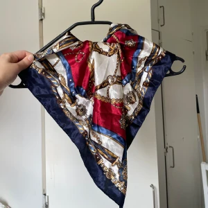 Silk scarf med kedjemönster - Snygg fyrkantig silk scarf med lyxigt kedje- och remmönster. Färgerna är marinblå, vinröd, vit och inslag av guld. Perfekt att knyta runt halsen eller i håret för en chic touch. Mjuk och glansig känsla som ger en elegant vibe.