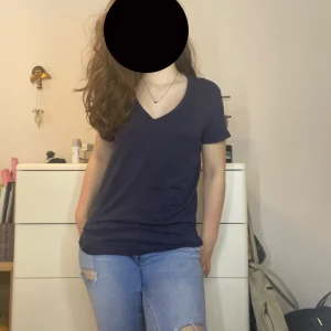 Mörkblå v-ringad t-shirt - Enkel och stilren mörkblå t-shirt med v-ringning och korta ärmar. Modellen är normalpassad och tillverkad i mjuk bomull, perfekt för en avslappnad look. Inga tryck eller mönster.