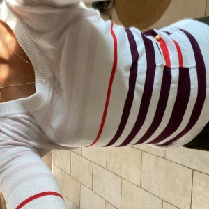 Randig tröja från Casall XS - Superfin  tröja från Casall i vitt med rosa, röda och mörklila ränder. Långärmad modell i xs med liten ficka framtill som har en guldfärgad knapp. Perfekt för dig som gillar färg och mönster. Snygg passform och rund halsringning. Litet hål under armen som bilden visar