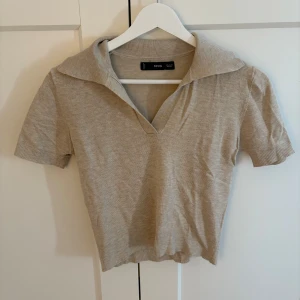 Beige stickad topp med krage från mango - Snygg beige stickad topp från mango med korta ärmar och bred krage. Toppen har v-ringning och ribbade kanter vid ärmslut och nederkant. Perfekt för dig som gillar en clean och stilren look.