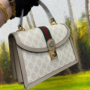 Guci beige handväska med GG-mönster - Snygg beige handväska från Guci med klassiskt GG-mönster, grönt och rött band mitt på och guldfärgat lås framtill. Väskan har stilrena kanter, topphandtag och är gjord i canvas med skinn-detaljer. Perfekt för dig som vill ha en ikonisk och trendig accessoar.