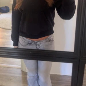 Grå bootcut jeans med broderade fickor - Säljer ett par grå jeans med bootcut-modell och snygga svarta broderier på bakfickorna. Jeansen har låg midja, klassisk femficksdesign och är tillverkade i mjukt denimtyg. Perfekta för dig som gillar en avslappnad men trendig look.