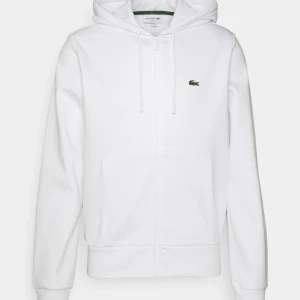 Vit hoodie från Lacoste med dragkedja - Vit hoodie från Lacoste med klassisk krokodil-logga på bröstet. Tröjan har knappt använts Max 1 gång, säljer pga den inte passade mig så bra 