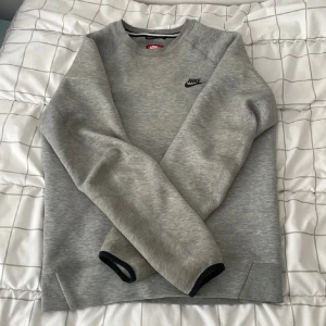 Grå Nike sweatshirt i bomull - Snygg grå sweatshirt från Nike med svart logga på bröstet. Tröjan har rund halsringning, långa ärmar och ribbade muddar. Perfekt för en chill och sportig stil. Tillverkad i mjuk bomullsmix som känns skön mot huden.