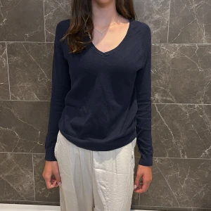 Mörkblå v-ringad tröja från Zara - Mörkblå v-ringad tröja från Zara i storlek L. Tröjan har lång ärm, ribbade muddar och är tillverkad i en mjuk mix av bomull och nylon. Enkel och stilren modell som passar perfekt till jeans eller kjol.