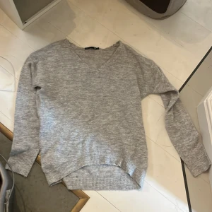 Grå v-ringad stickad tröja 157 - Mysig grå stickad tröja från 157 i storlek S. Tröjan har v-ringning, långa ärmar och ribbade muddar vid ärmslut och nederkant. Perfekt för lager-på-lager och chill dagar. Enkel att matcha med jeans eller kjol.