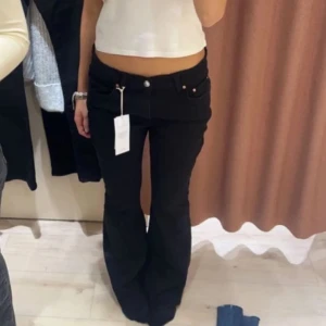 Svarta bootcut jeans - Snygga svarta bootcut jeans med mid midja. Perfekta för en trendig look. De har en klassisk design med fickor och knappar framtill. En liten fläck på låret. Färgen är lite ur tvättad