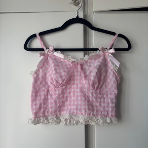 Rutig rosa linnetopp med spets - Supersöt rosa och vit rutig linnetopp med spetskant och volang nertill från SHEIN. Dekorerad med små rosetter i satin och smala axelband. Perfekt för dig som gillar gulliga detaljer och romantisk stil. Hör av dig om du vill ha fler bilder eller har några frågor! 