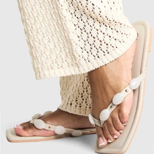 Vita sandaler med pärldetaljer från Boohoo - Stilrena vita sandaler från Boohoo med fyrkantig tå och dekorativa vita pärlor på remmarna. Snygg minimalistisk design med platt sula, perfekt för en trendig look. Tillverkade i syntetmaterial. Endast testade en gång utomhus men tyvärr lite förstora för mig. Passar en 40 bättre.