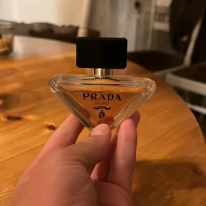 Prada Milano parfym - Exklusiv parfym från Prada Milano i en unik, triangelformad glasflaska med svart och guld kork. Flaskan har en elegant design med genomskinligt glas och ljus bärnstensfärgad vätska. Perfekt för dig som gillar lyxiga och stilrena dofter. 