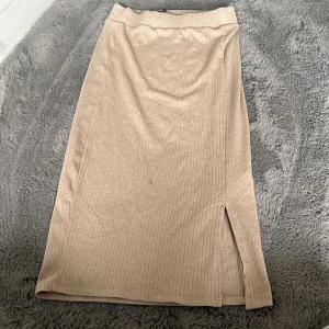 Beige ribbad långkjol från LMTD - Snygg beige långkjol från LMTD i ribbad bomull med en liten slits på sidan. Kjolen har en enkel och clean look som är lätt att matcha med olika toppar och sneakers. Perfekt för dig som gillar en chill och stilren vibe.