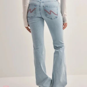 Low waist bootcut jeans - Säljer ett par ljusblå bootcut jeans med slitna knän och snygga broderade detaljer på bakfickorna. Lågmidjade från Nelly! Knappt använda