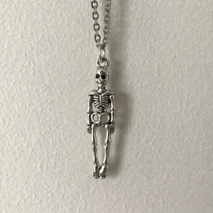 Halsband med skelettberlock - Unikt halsband med en detaljerad skelettberlock i silverfärg. Kedjan är tunn och elegant, vilket gör att berlocken verkligen står ut. Perfekt för att ge en edgy touch till din stil.