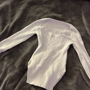 Vit ribbad topp - Säljer en stilren vit ribbad topp med långa ärmar. Toppen har en elegant design med en subtil struktur som ger en snygg look. Perfekt för att matcha med olika outfits.