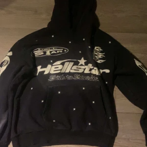 Svart Hellstar Hoodie - Säljer en svart hoodie från Hellstar med coolt tryck av stjärnor och flammor i vitt. Hoodien har en klassisk passform med lång ärm och en stor ficka framtill. Perfekt för dig som vill ha en unik stil!