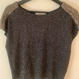 Glittrig topp från Zara med fina detaljer på axlarna. - Snygg glittrig topp från Zara med korta ärmar och ett unikt mönster på axlarna. Perfekt för att lysa upp vilken outfit som helst. Den har en bekväm passform och är lätt att matcha med olika stilar.