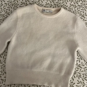 Vit stickad tröja från Zara - Säljer en stilren vit stickad tröja från Zara. Tröjan har en croppad design med ribbade kanter och korta ärmar. Perfekt för en avslappnad look. Passar bra till jeans eller kjol. (Även bild på mig från en TikTok)