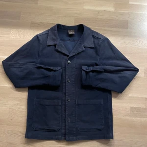 Overshirt Oscar Jacobsson - Snygg mörkblå overshirt från Oscar Jacobson. Materialet är mjukt och skönt. Som det syns i annonsen så är färgen lite sliten men det skapar en skön vintage känsla. Skriv för frågor!