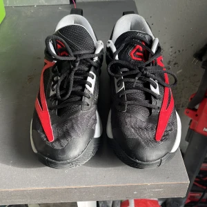 Svarta och röda sneakers från Nike - Snygga svarta sneakers med röda detaljer från Nike. Skorna har en sportig design med snörning och en bekväm sula. Perfekta för en aktiv livsstil.