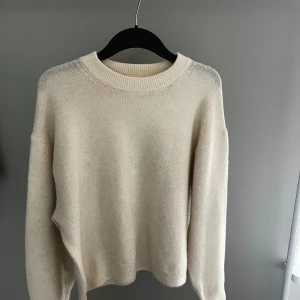 Beige stickad tröja från H&M - Säljer en stilren beige stickad tröja från H&M. Tröjan har en rund halsringning och långa ärmar, perfekt för kyligare dagar. Enkel och tidlös design som passar till det mesta. 