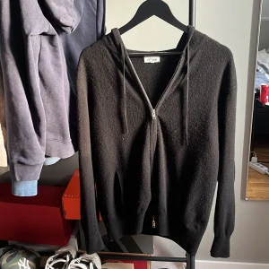 Svart hoodie från Soft Goat - Säljer en stilren svart hoodie från Soft Goat. Den har dragkedja framtill och en bekväm huva med snörning. Perfekt för kyliga dagar och passar till det mesta i garderoben.