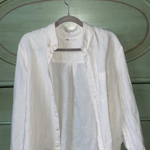 Vit linneskjorta från Zara - Snygg vit skjorta i linne från Zara med klassisk krage och knappar framtill. Perfekt för en stilren look. Skjortan har långa ärmar och en bröstficka för extra stilpoäng. Tvär snyggt att ha på en varm sommar dag!