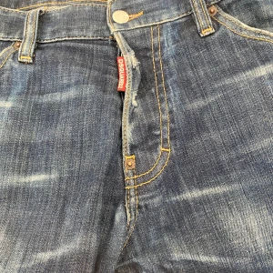 Blå jeansbyxor från Dsquared2 - Snygga blå jeansbyxor från Dsquared2 med en klassisk femficksdesign och slitna detaljer. Byxorna har en knappgylf och en läderpatch med logotyp baktill. Perfekta för en avslappnad stil.