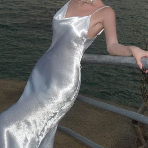 Maxi klänning  - Säljer en elegant silverfärgad långklänning i satin med smala axelband och en vacker öppen rygg. Klänningen har en stilren design och en glansig finish som ger en lyxig känsla. Perfekt för speciella tillfällen! ✨