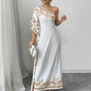 Vit one-shoulder klänning med broderier - Elegant vit långklänning med one-shoulder design och vackra broderier i guld längs kanten. Perfekt för speciella tillfällen med sin flytande siluett och unika stil.
